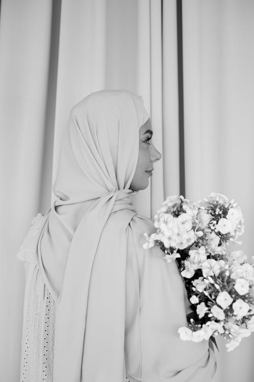 Free Grayscale Photo of Woman in White Hijab Holding Bouquet of Flowers Stock Photo