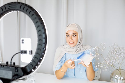 A young Muslim woman using her phone to record a video indoors, with a ring light.