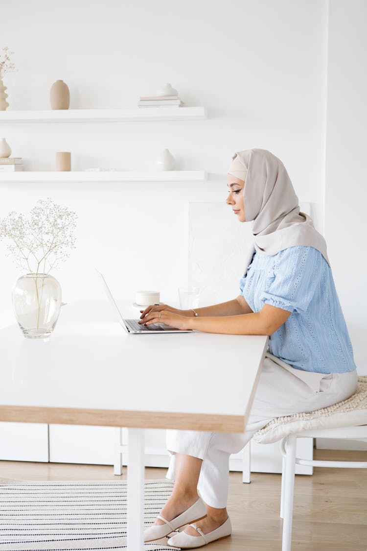 Woman In Blue Shirt And White Pants Using Laptop