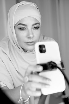 Muslim woman wearing hijab engaged in vlogging with a smartphone.
