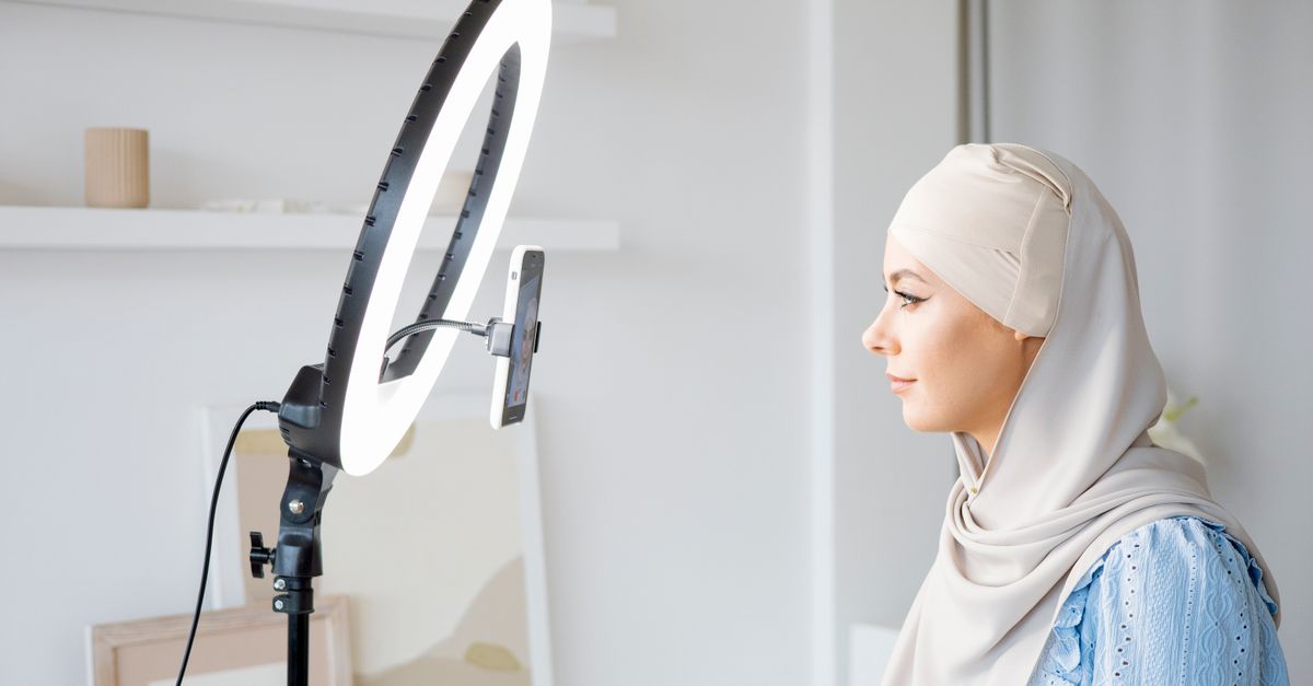 A woman in hijab uses ring light for video content creation indoors.