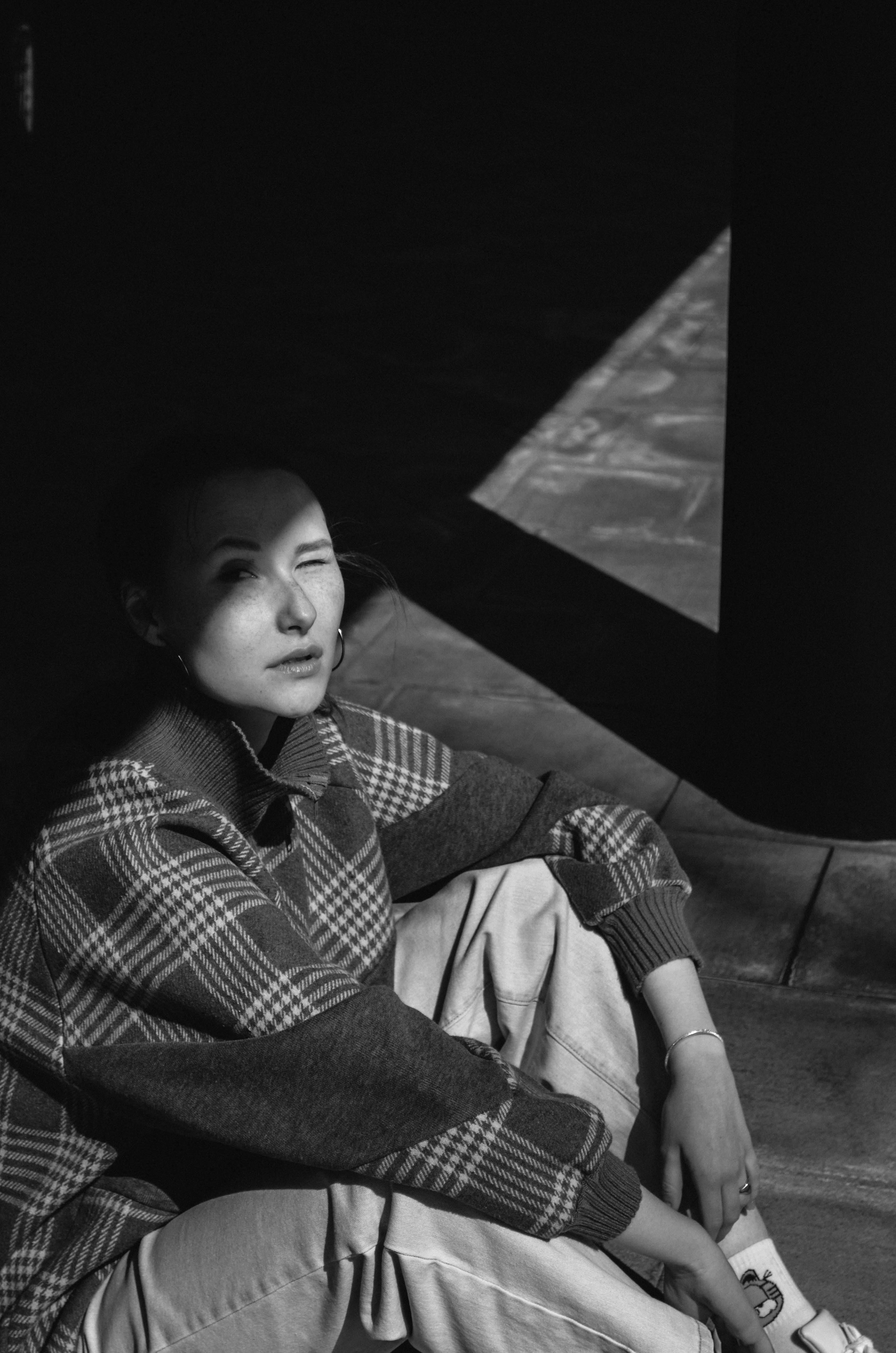 Artistic black and white photo of a woman winking in shadows, highlighting emotions.