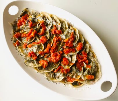 Delicious homemade dumplings topped with fresh tomato salsa and herbs on a white platter.