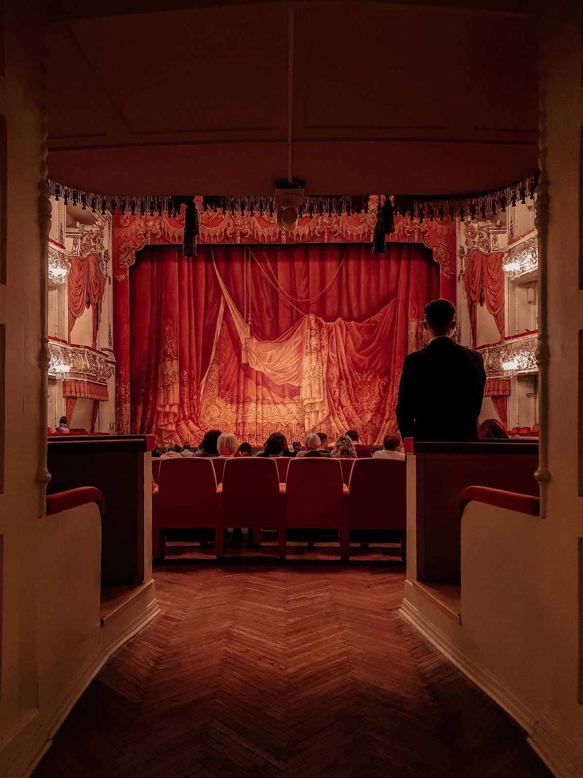 Theater interior with red velvet curtains and seated audience