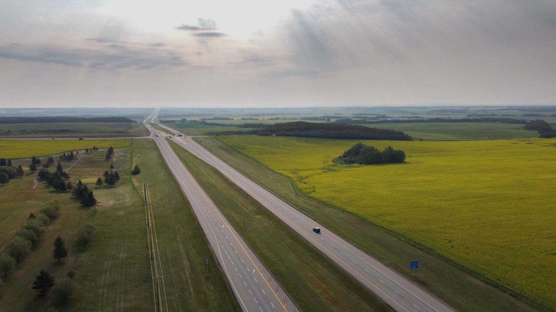 Stunning aerial view of Sylvan Lake highway with expansive fields under a summer sky.