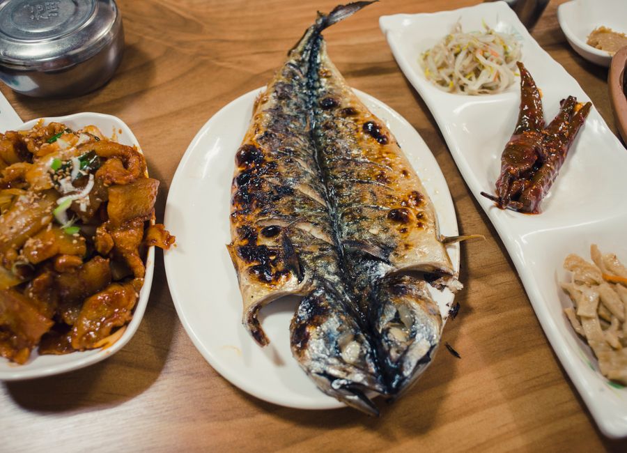 A delicious Korean dinner featuring grilled saba fish, side dishes, and a wooden table setting.