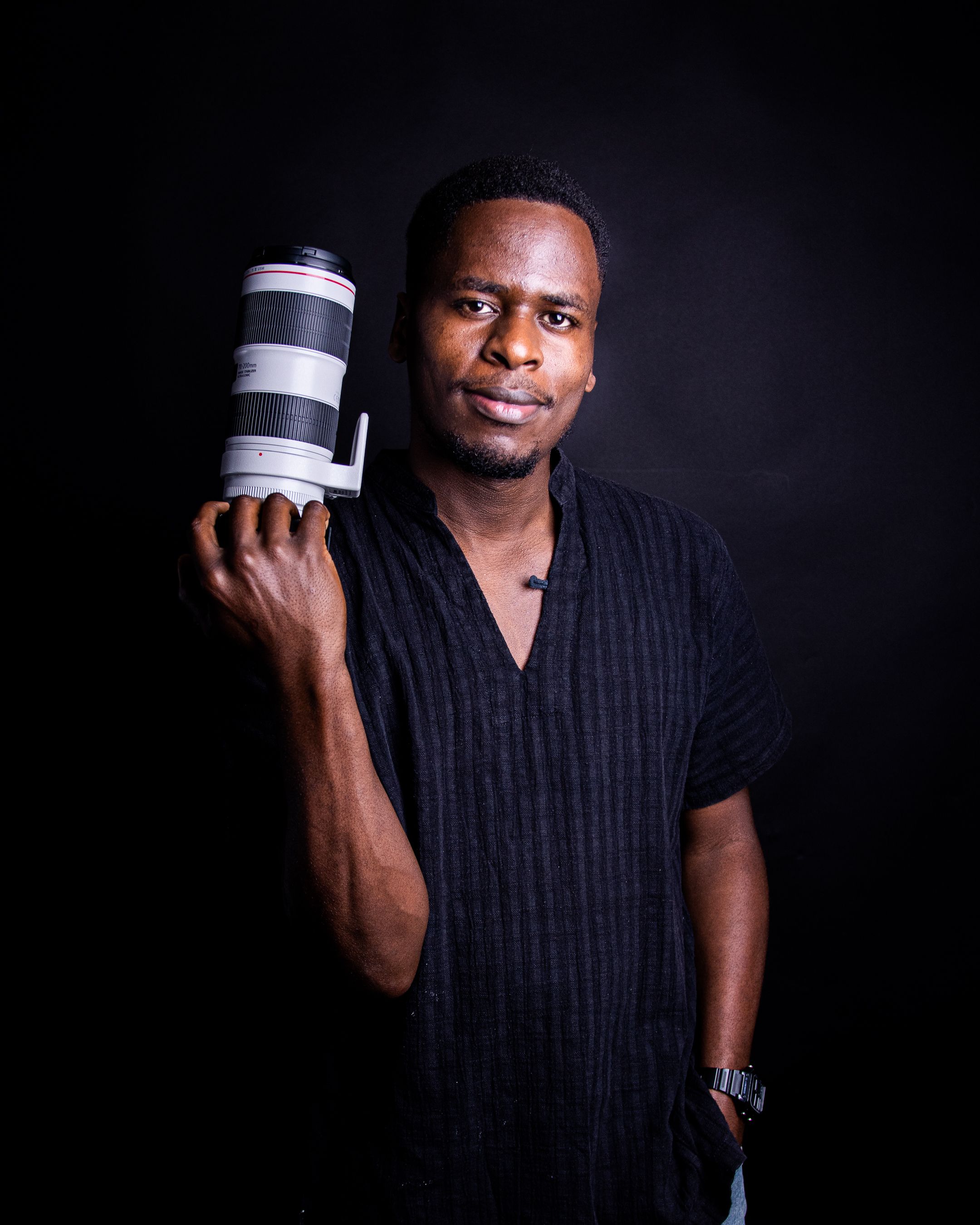 A confident African man holding a professional camera lens in a studio setting.
