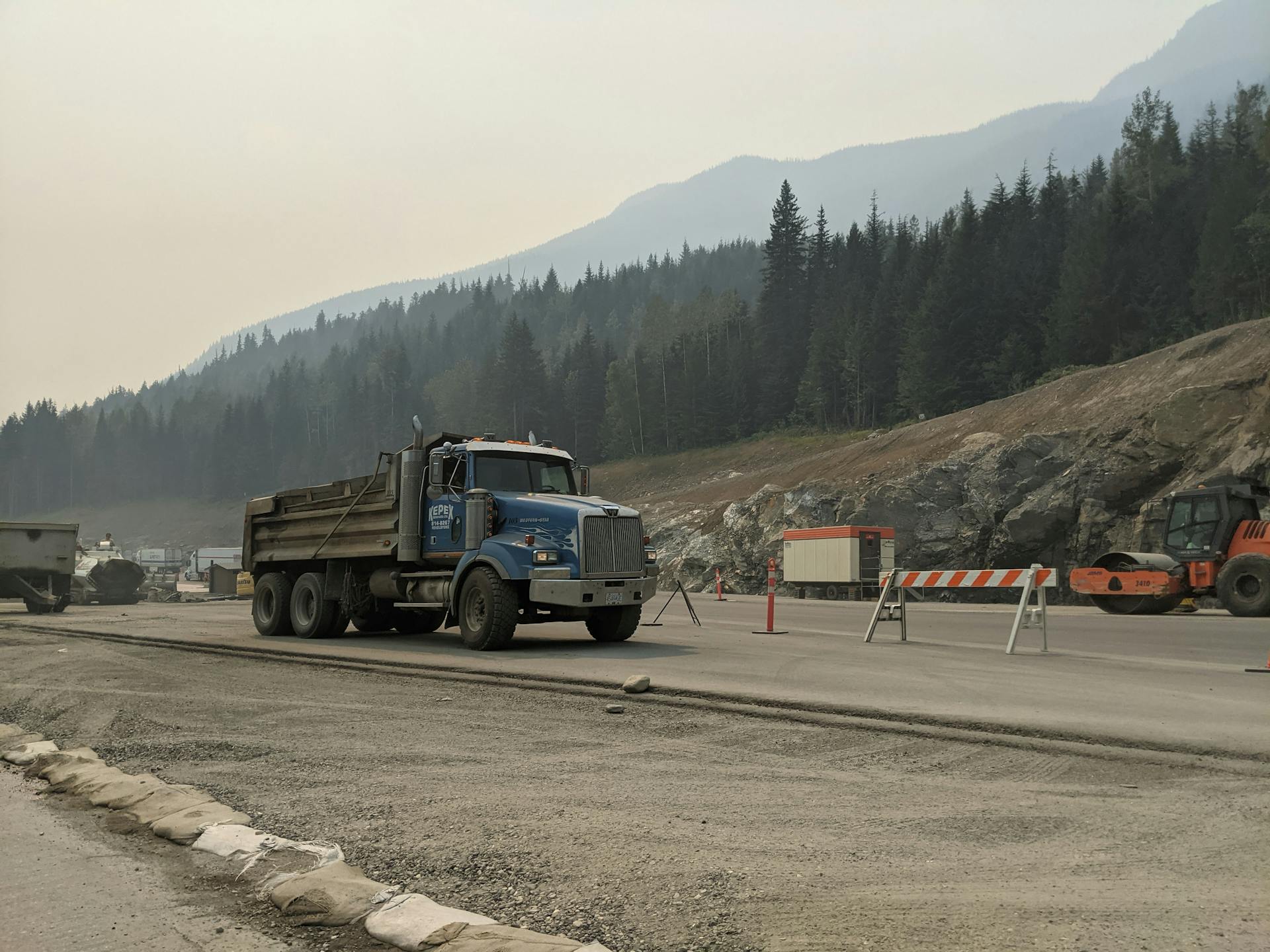 A construction truck working on a mountain road amidst heavy machinery and equipment.