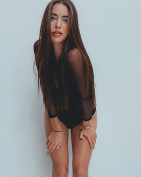 Woman in black outfit posing with hands on knees against plain background.