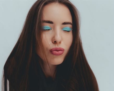 Studio portrait of a woman with vibrant blue eye shadow and pouting lips, eyes closed.