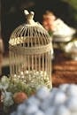 这款迷人的复古鸟笼饰有珍珠，周围环绕着鲜花，是完美的婚礼装饰