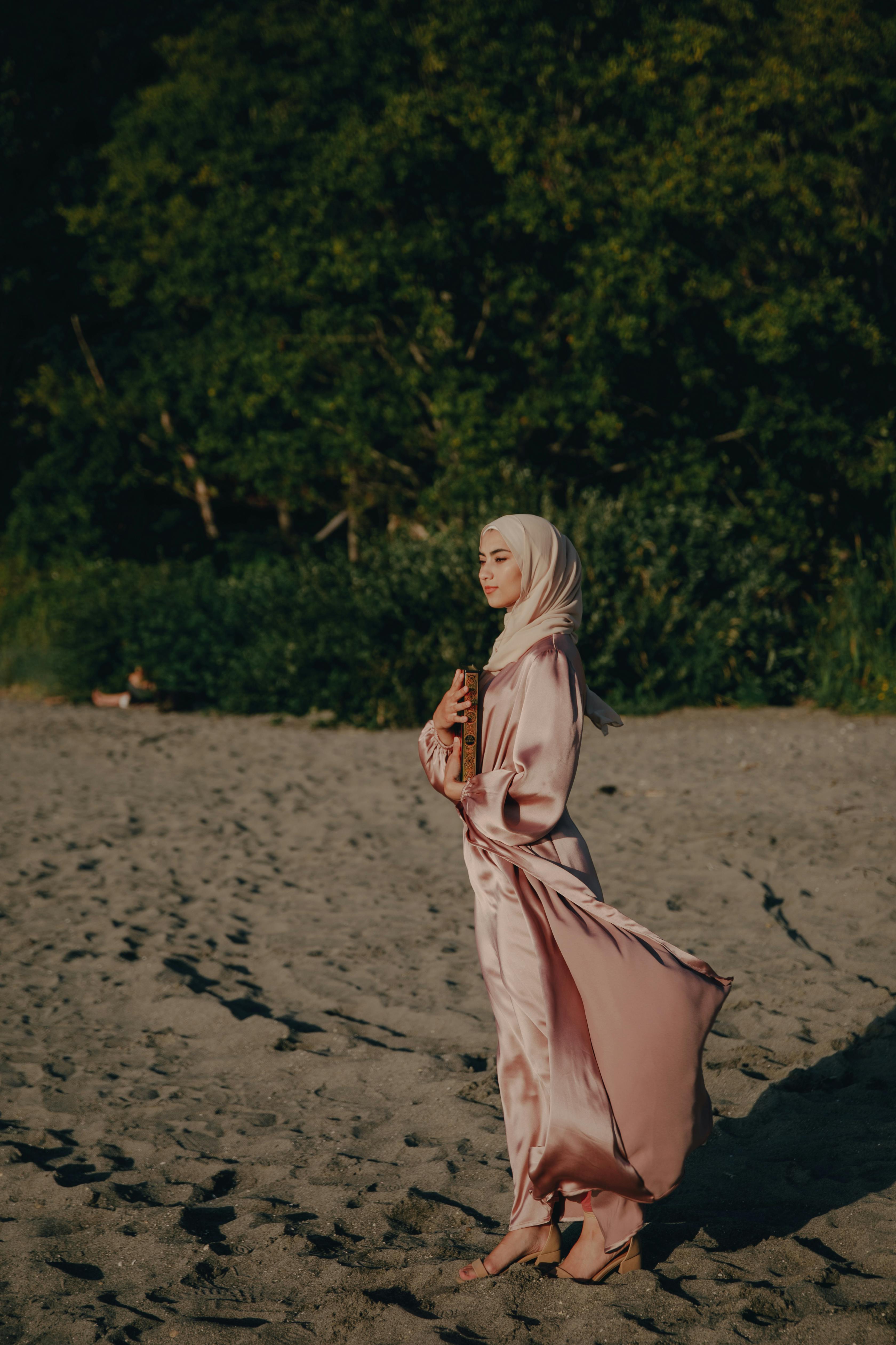 woman in hijab and pink silky dress standing on the beach