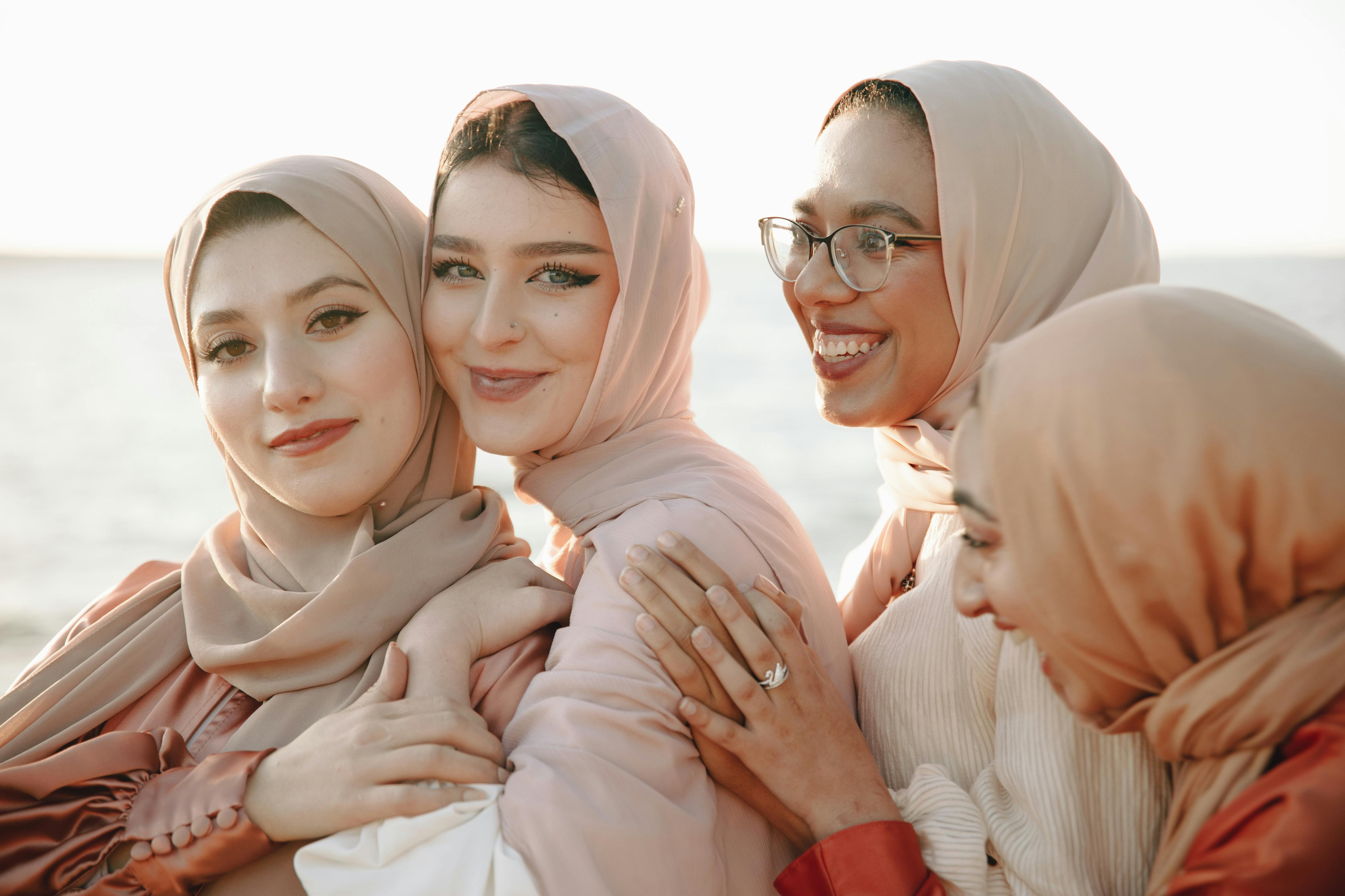 A group of smiling women in hijabs enjoying a sunny day by the sea, embracing diversity and friendship.