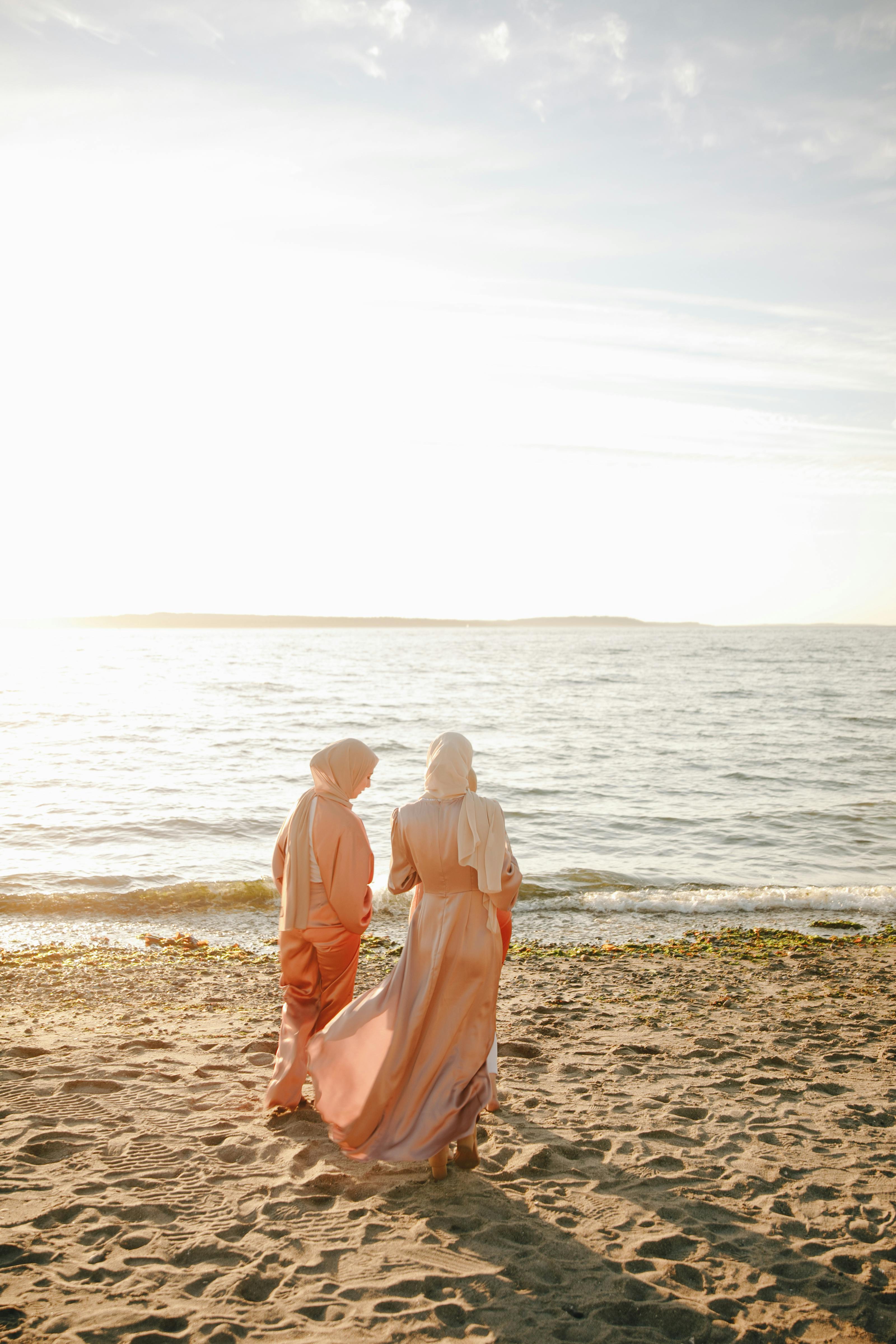 two women in traditional dress and hijab standing on beach