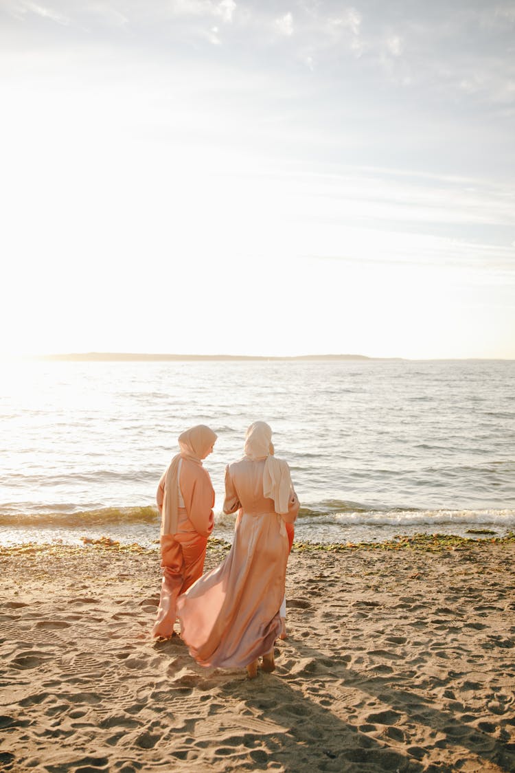 Two Women In Traditional Dress And Hijab  Standing On Beach