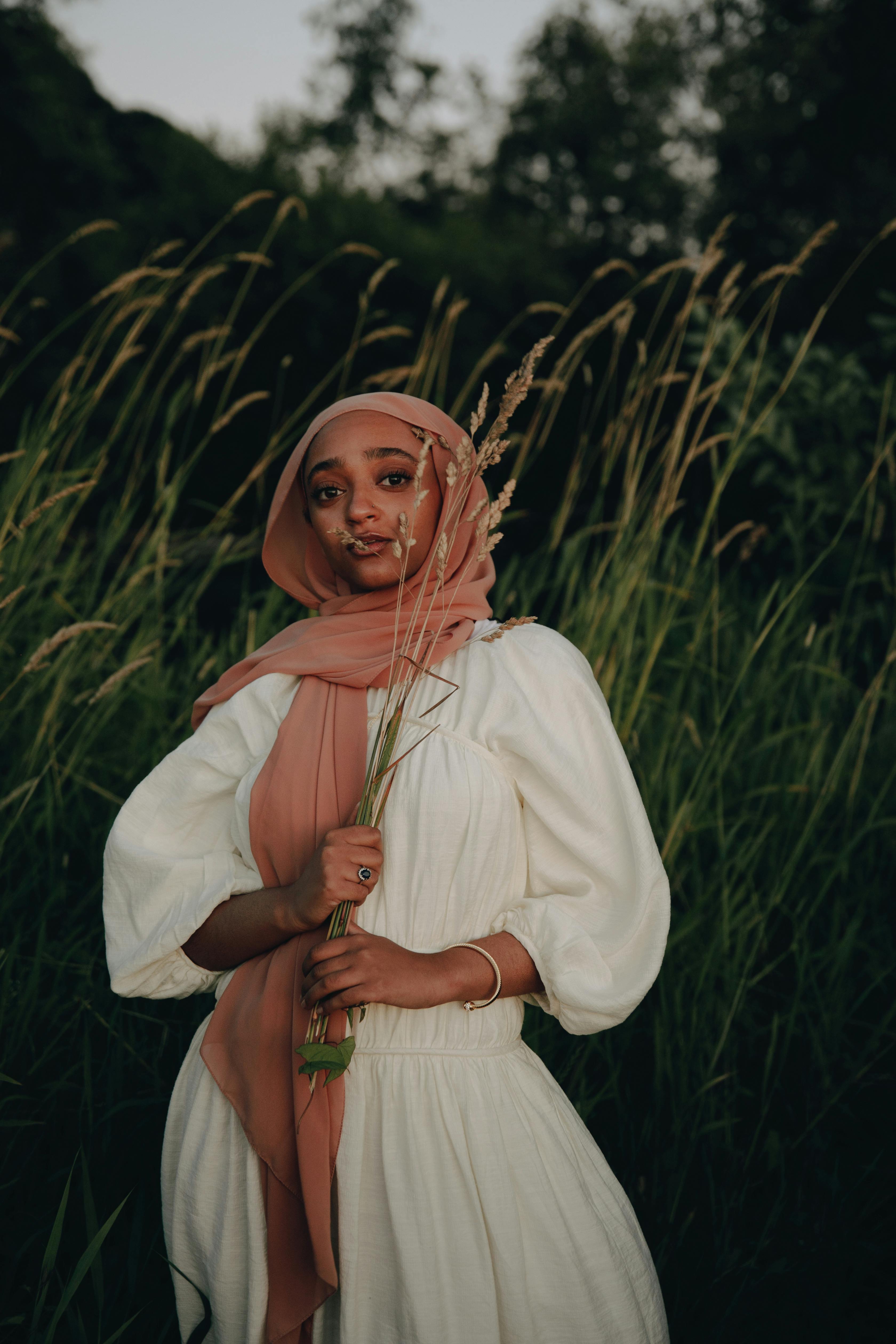 A woman in a hijab poses gracefully in a wheat field, embodying peace and elegance.