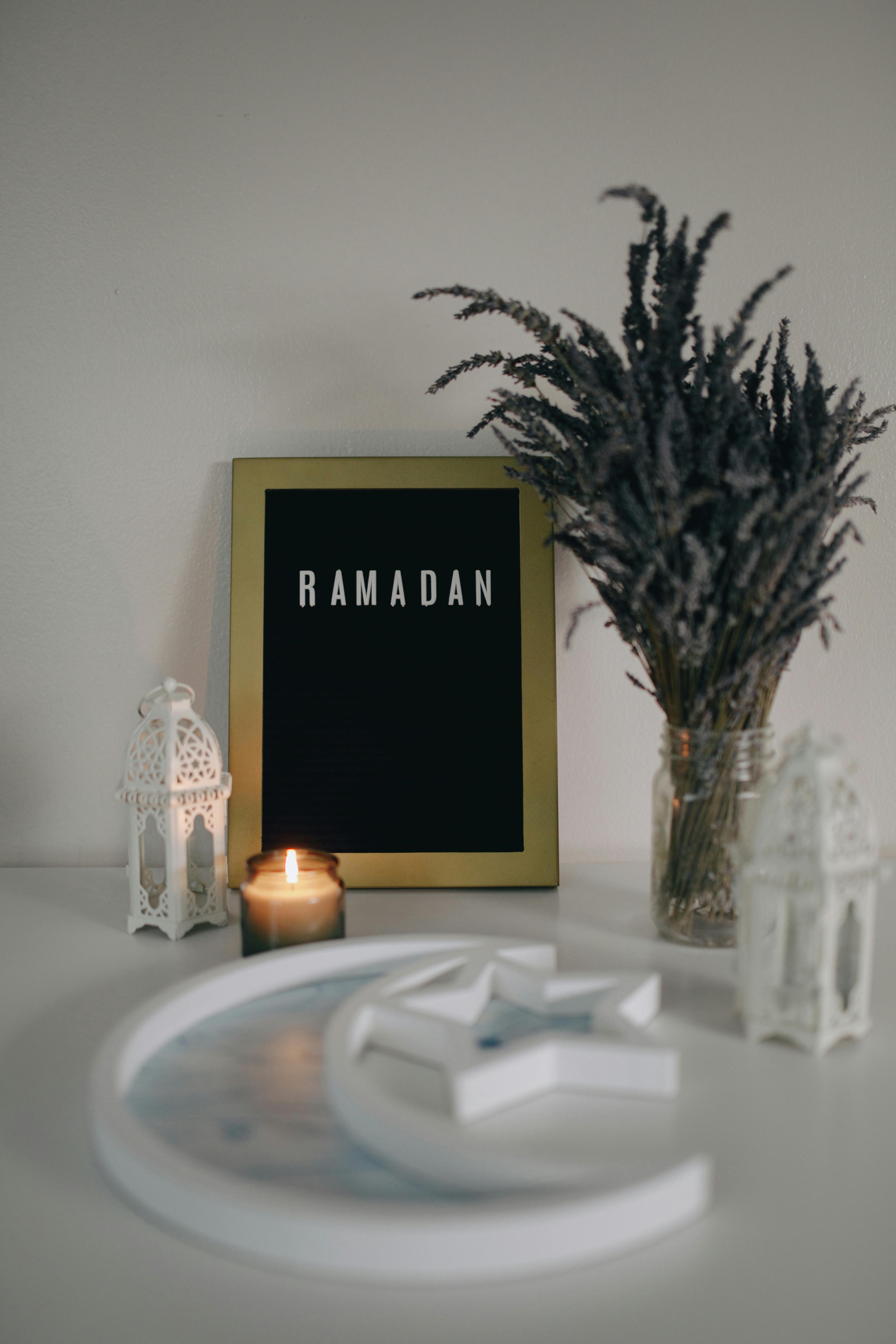 a ramadan word on a picture frame beside dried leaves and a candle light