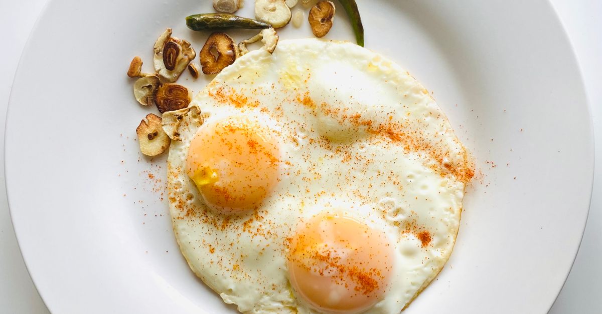 Appetizing fried eggs sprinkled with spices and garnished with fried garlic and green chili on a white plate. - Evidence evidence guide for garlic cholesterol meta-analysis