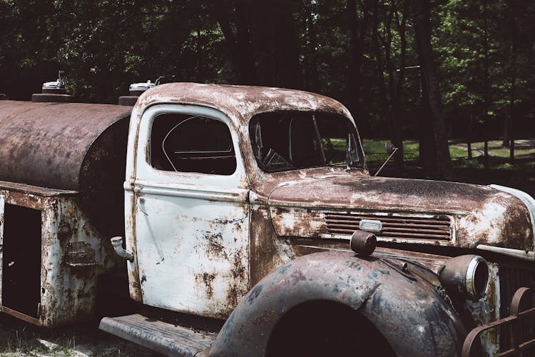 A Broken Rusty Car Parked Near Trees