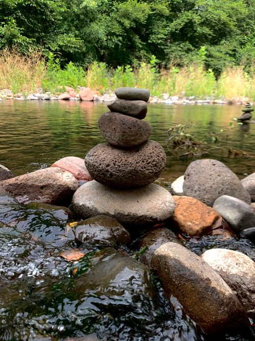 Free Balanced stone stack by a peaceful river in a lush forest setting. Stock Photo