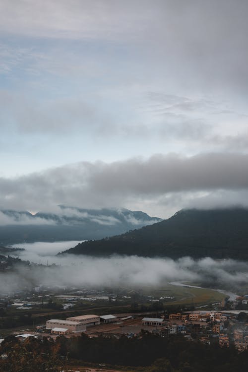 Aerial View of Buildings Near Mountain Under White Clouds