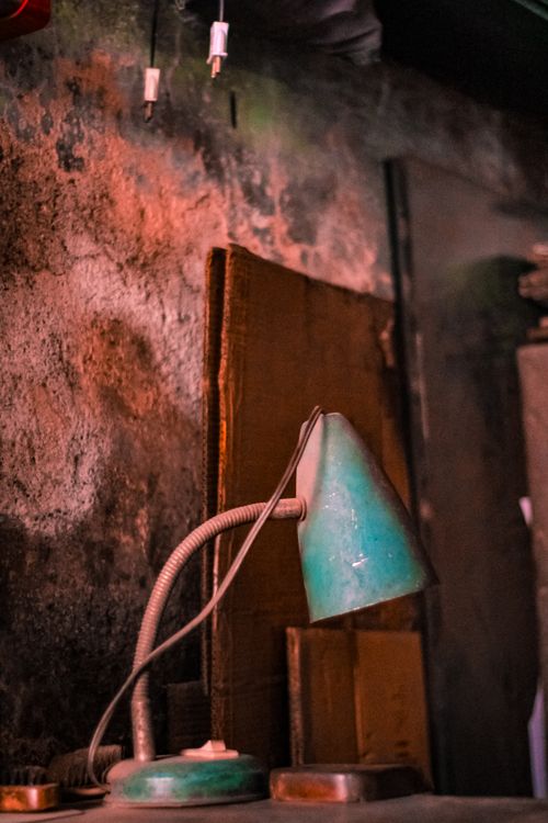 Free An old green desk lamp against a weathered wall, evoking a vintage rustic feel. Stock Photo