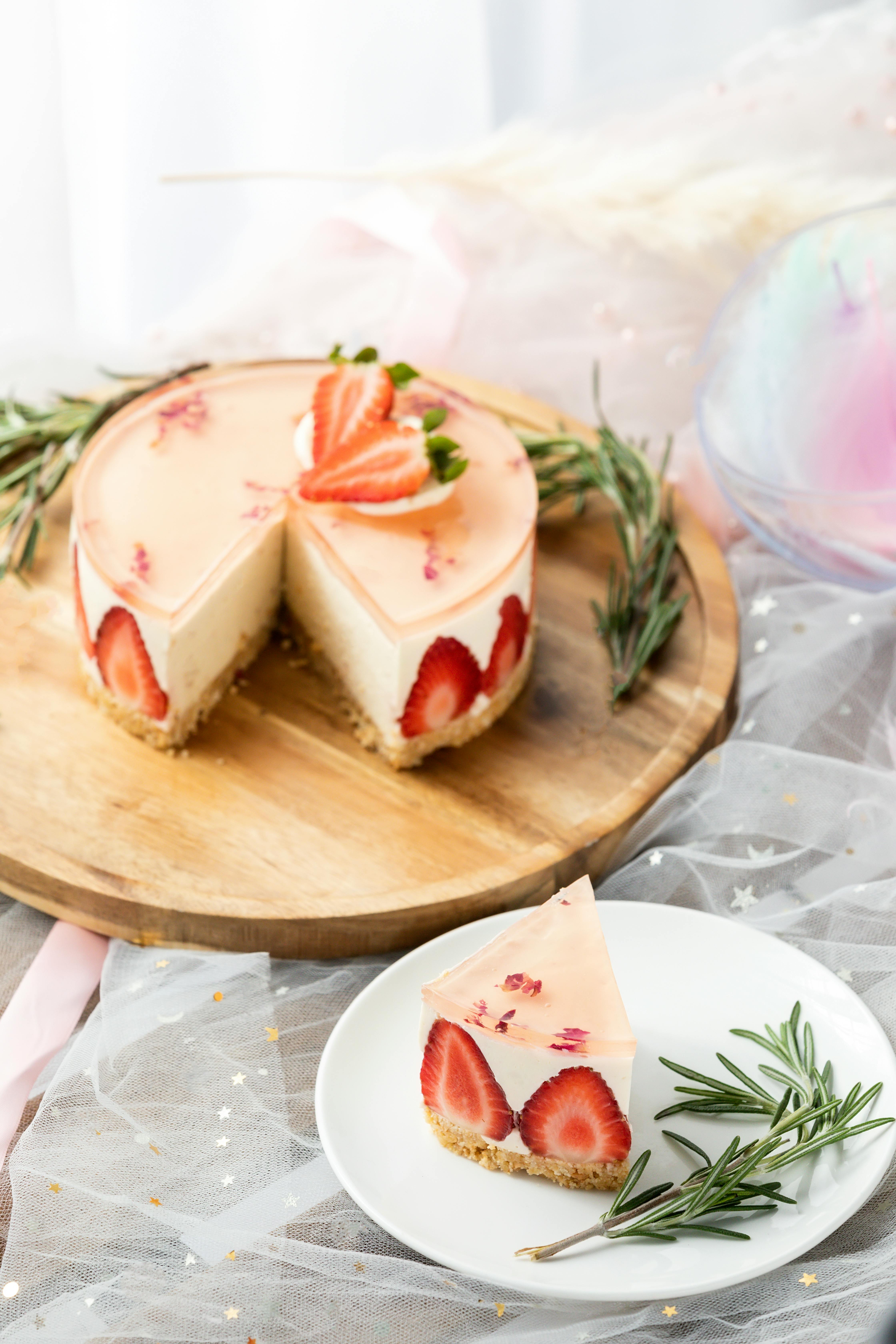 Mouthwatering strawberry cheesecake slice with rosemary garnish on a wooden board.