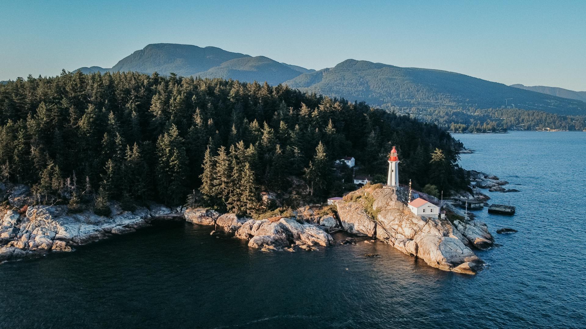 Aerial view of a lighthouse on rocky shoreline surrounded by forest in West Vancouver, BC, Canada.