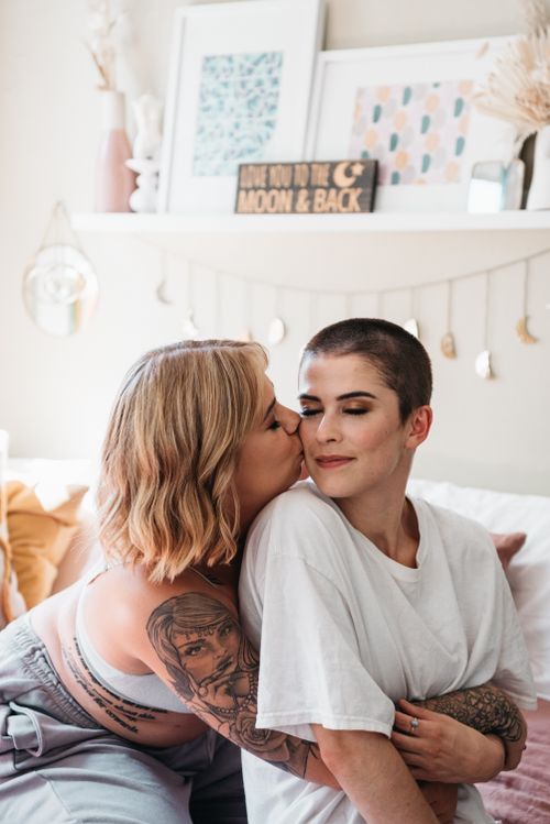 Free Affectionate LGBTQ couple embracing in a cozy bedroom setting with decor. Stock Photo