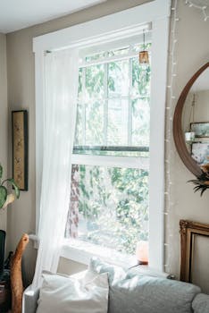 A cozy indoor corner featuring a bright window, sheer curtains, and lush greenery.