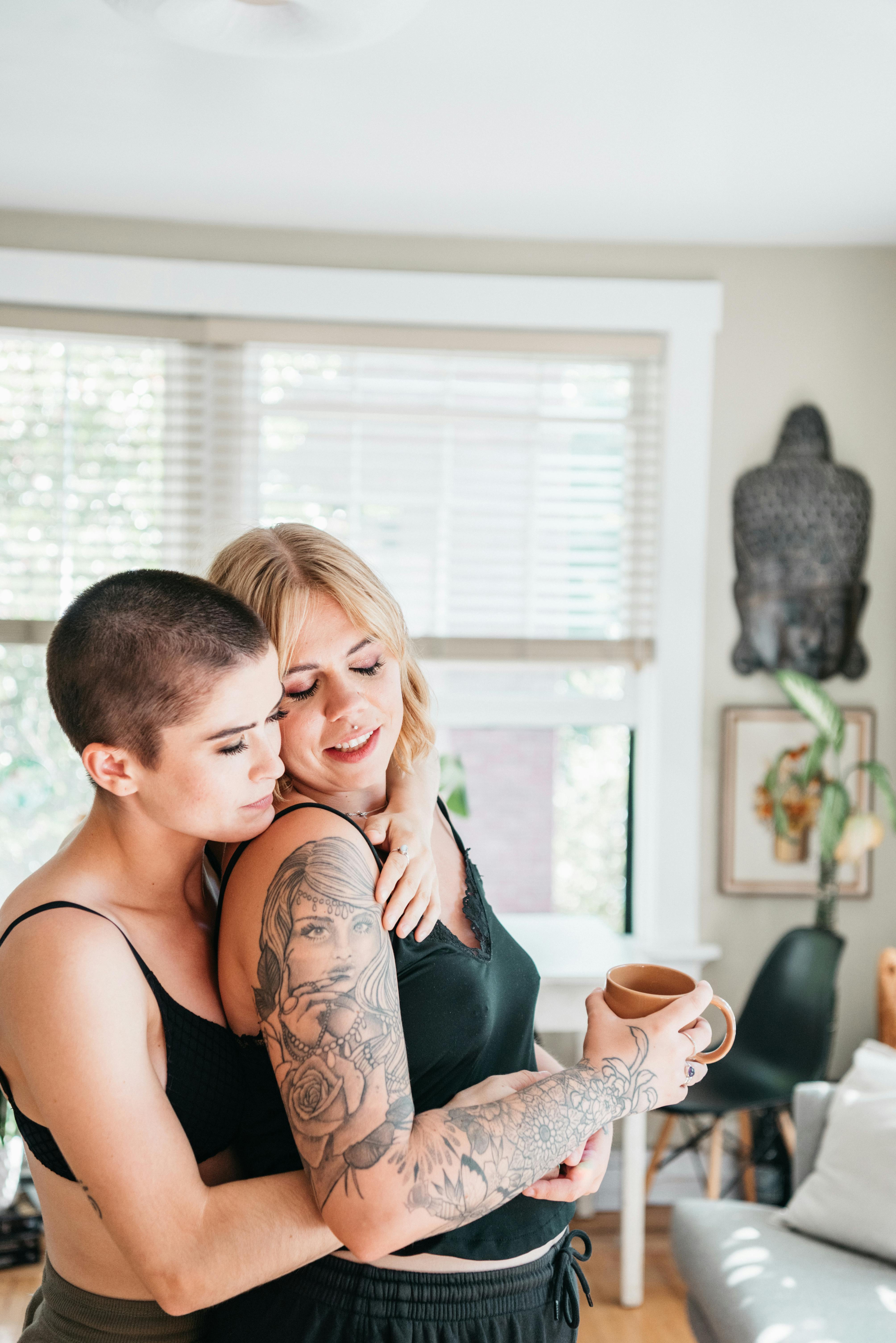 woman wearing black brassiere hugging another woman