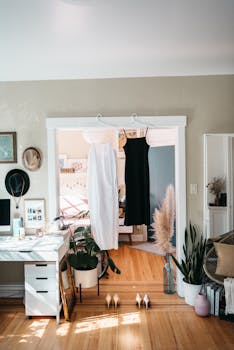 Elegant bedroom interior with black and white dresses hanging, surrounded by plants and fashion decor.