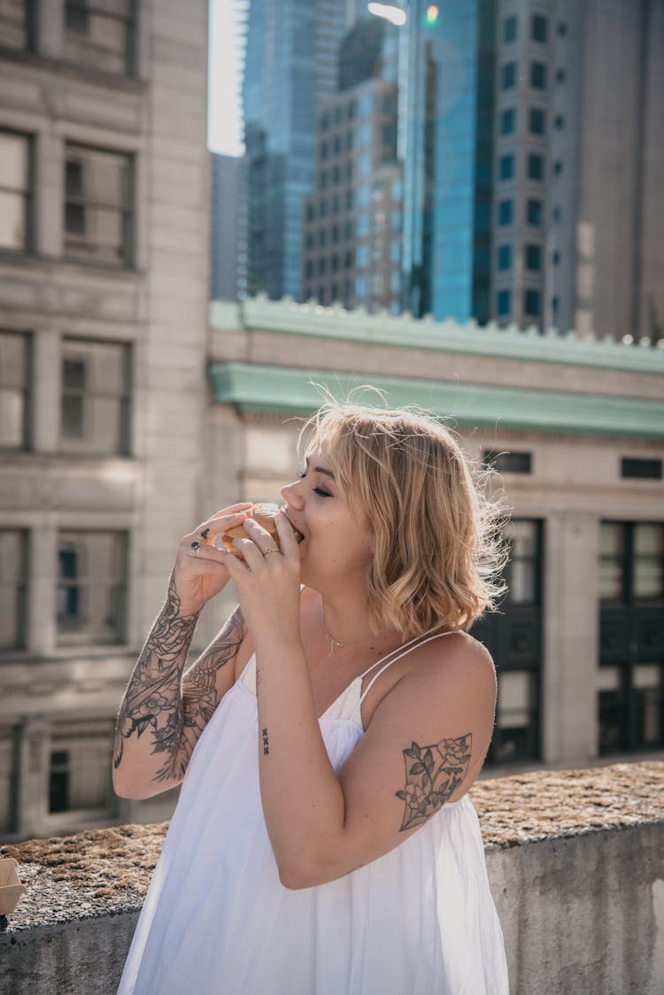 A Woman In White Tank Top On The Roof Top Eating A Burger