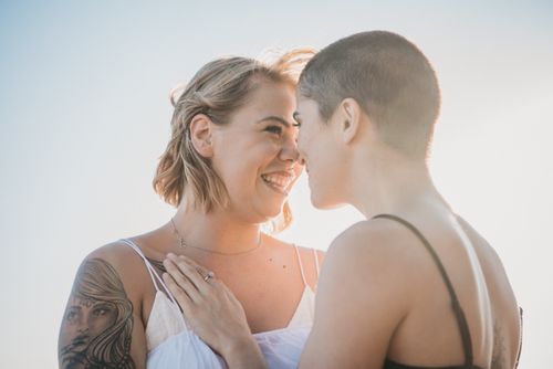Free A smiling LGBTQ couple sharing an intimate moment outdoors under bright sunlight. Stock Photo