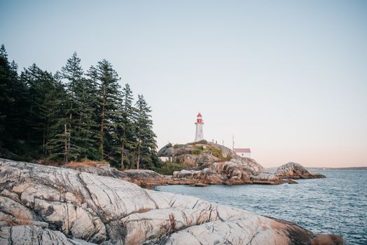 Tranquil coastal scene with a lighthouse overlooking rocky formations and the ocean during sunset.