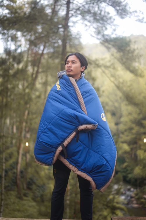 Free A serene moment of a man wrapped in a vibrant blue blanket, enjoying a peaceful forest setting. Stock Photo