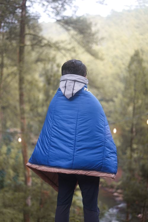 Free Adult wrapped in a blue sleeping bag standing in a forest, looking towards trees. Stock Photo