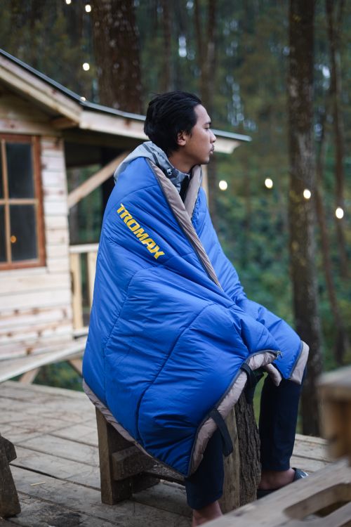 Free Man enjoying a quiet moment wrapped in a sleeping bag on a rustic cabin porch. Stock Photo