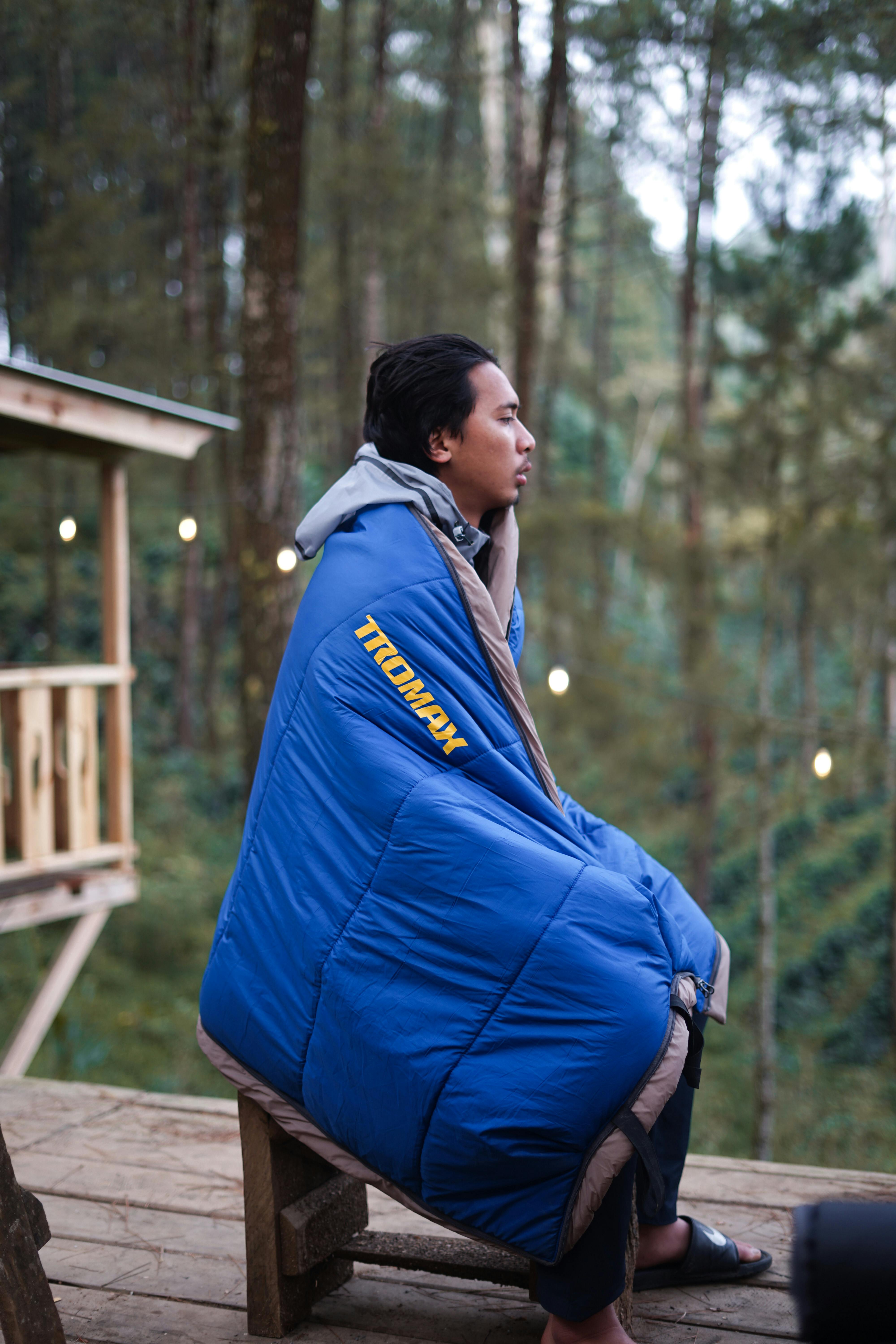 REI HunkerDown 20 sleeping bag laid out on a campsite picnic table with pine trees in the background