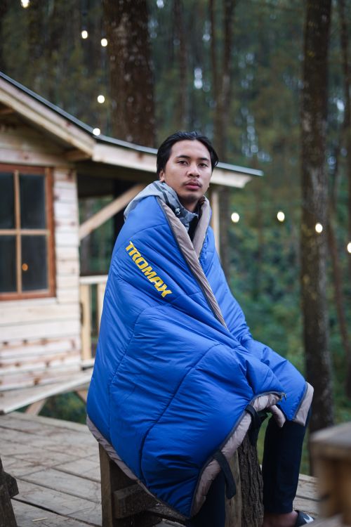Free Man wrapped in a blue blanket sitting outside a tree house with trees in the background. Stock Photo