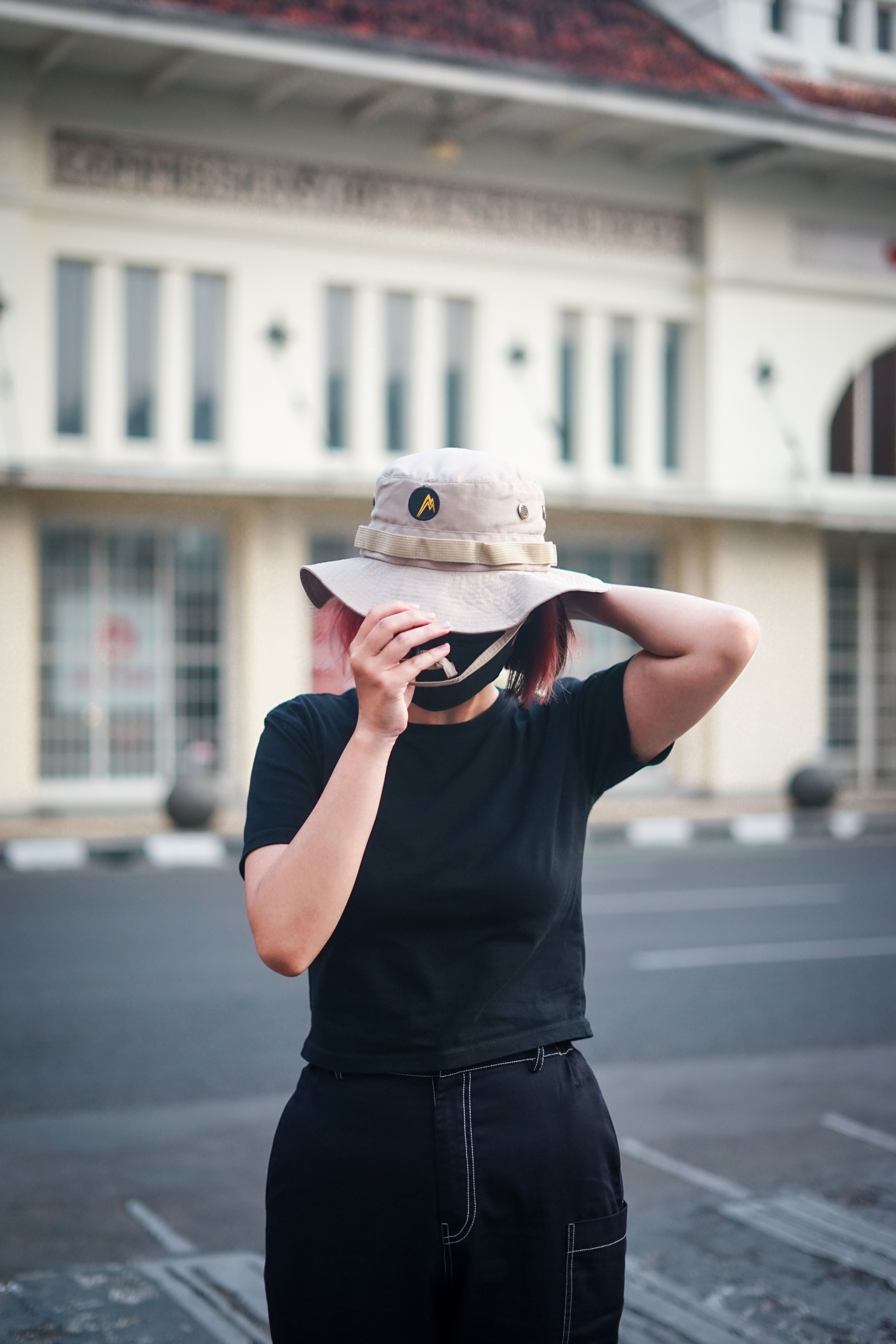 A woman adjusts her bucket hat while standing in an urban outdoor setting.