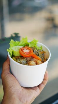 Close-up of a fresh salad in a takeaway container held by hand, highlighting its vibrant ingredients.