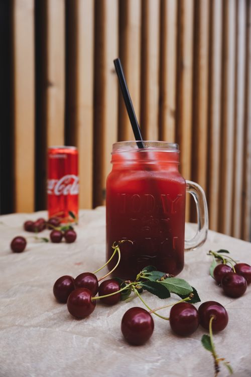 Free Mason jar of cherry juice and Coca-Cola can on a table with fresh cherries. Stock Photo