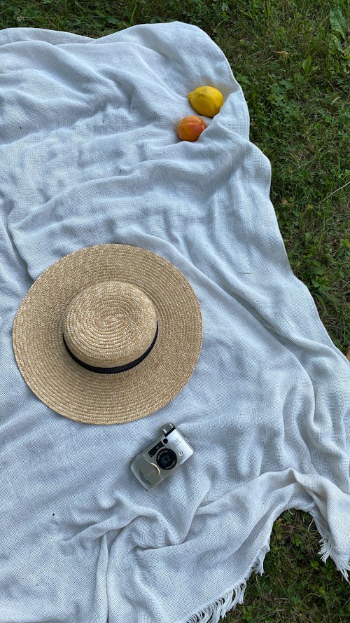 Brown Straw Hat Beside Camera on White Cloth