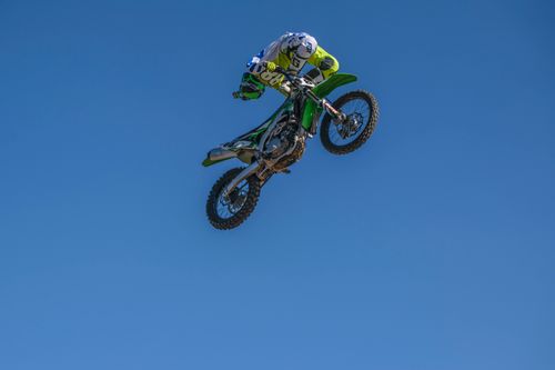 Free Exciting motocross stunt performed by a rider in mid-air against a clear blue sky, showcasing skill and agility. Stock Photo