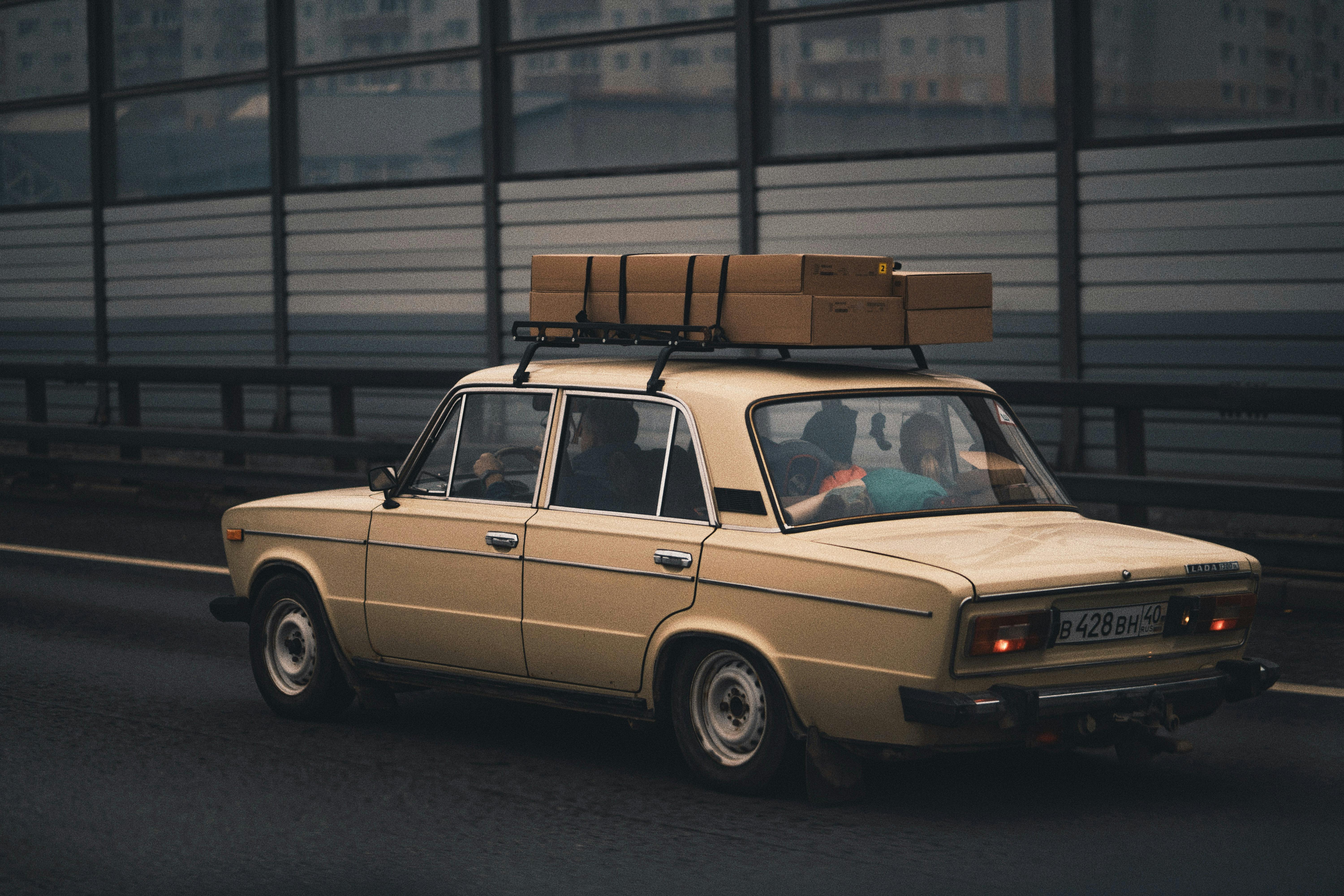 Free Classic beige sedan carrying luggage, driving on highway with city in background. Stock Photo