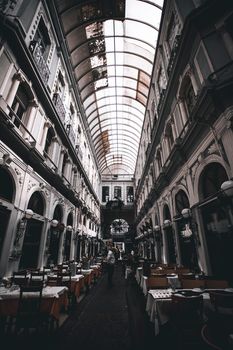 Explore a grand arcade with classical architecture housing a charming indoor restaurant setting.