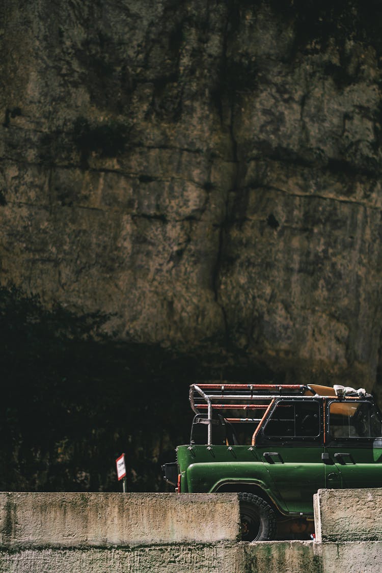 Green Jeep Parked Under Stone Wall