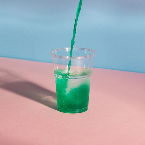 Free Vibrant green liquid being poured into a clear plastic cup against a pastel background. Stock Photo
