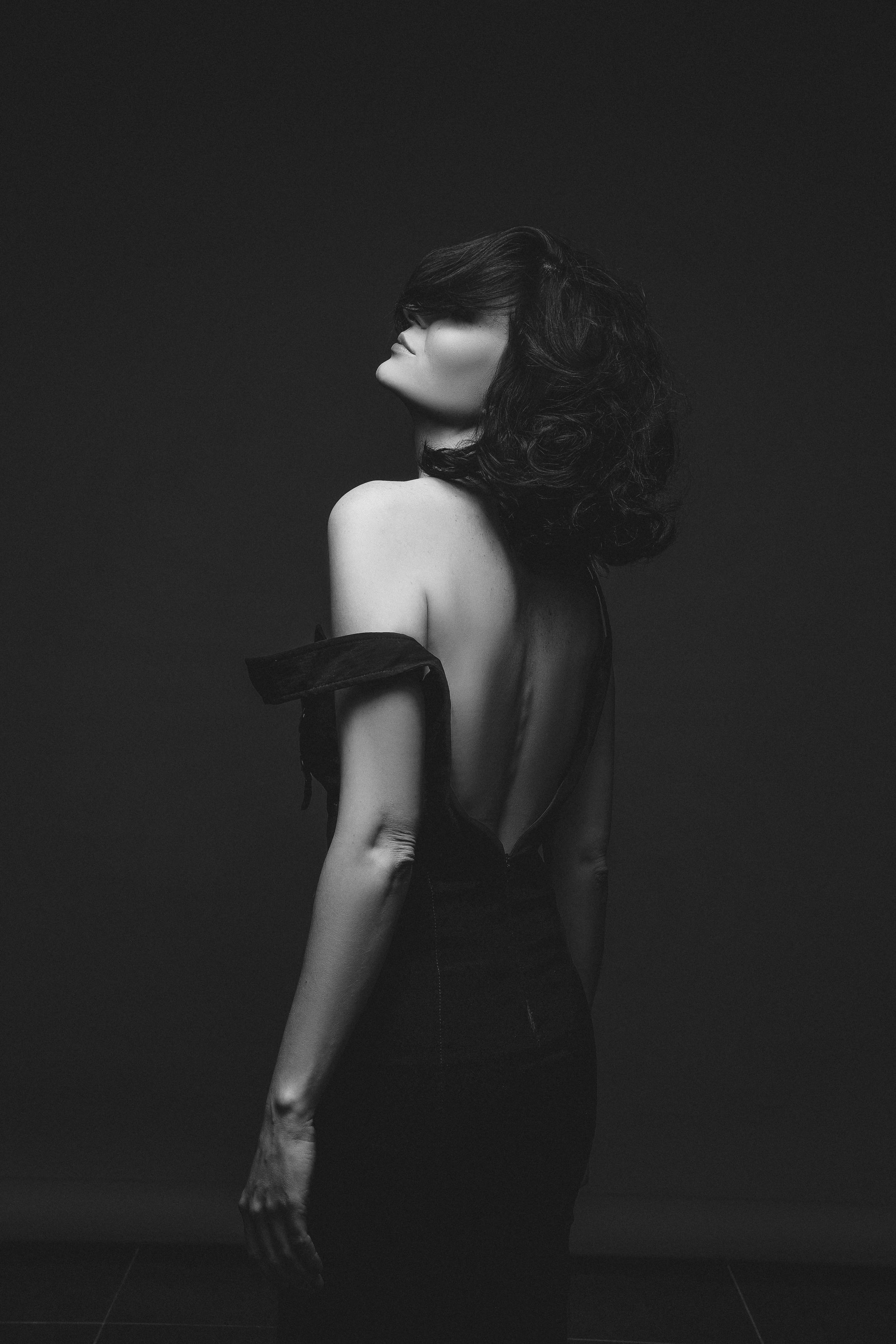 Elegant black and white portrait of an adult woman in an off-shoulder dress, studio setup.
